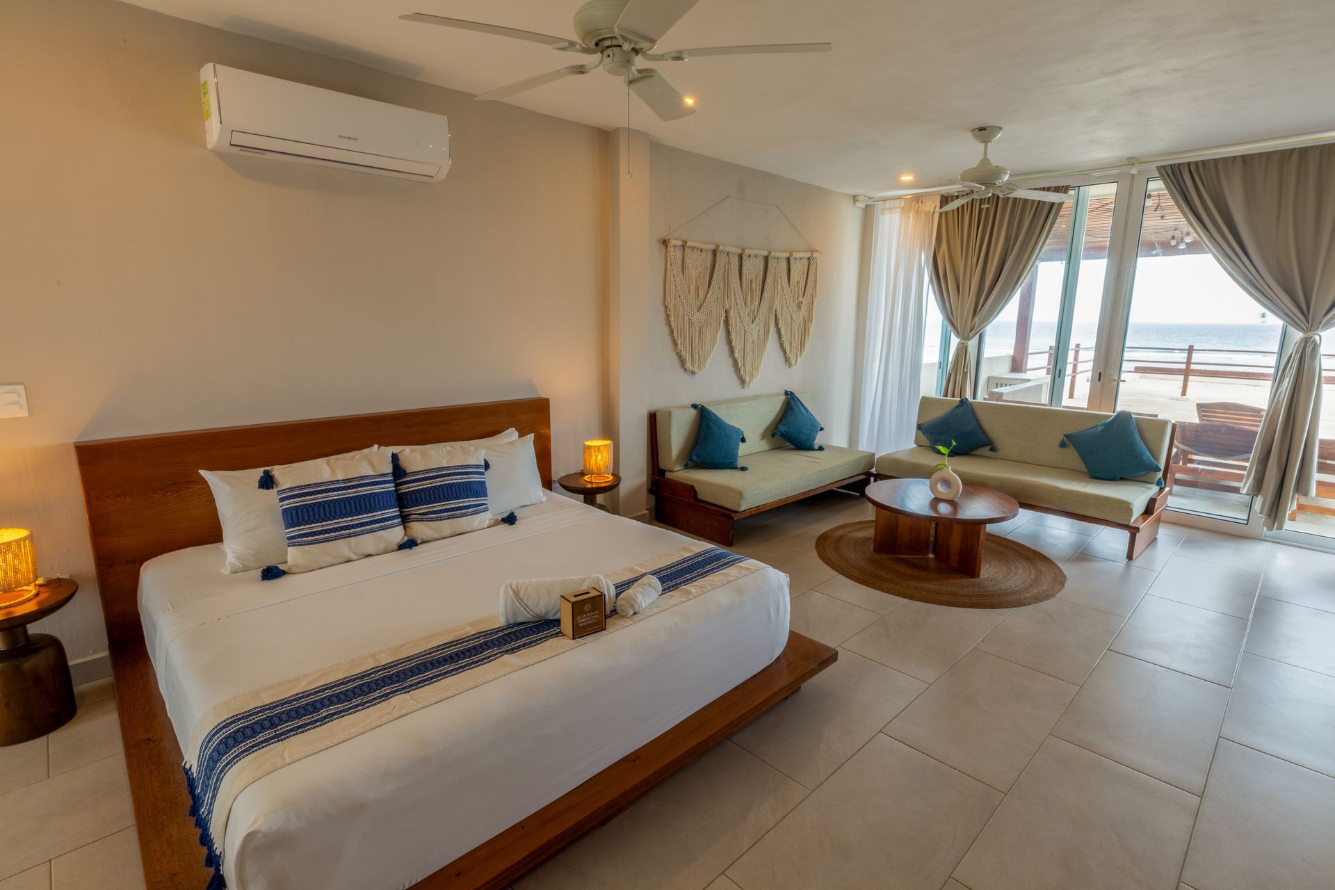 Habitación luminosa con cama, sofá y balcón con vistas al agua.