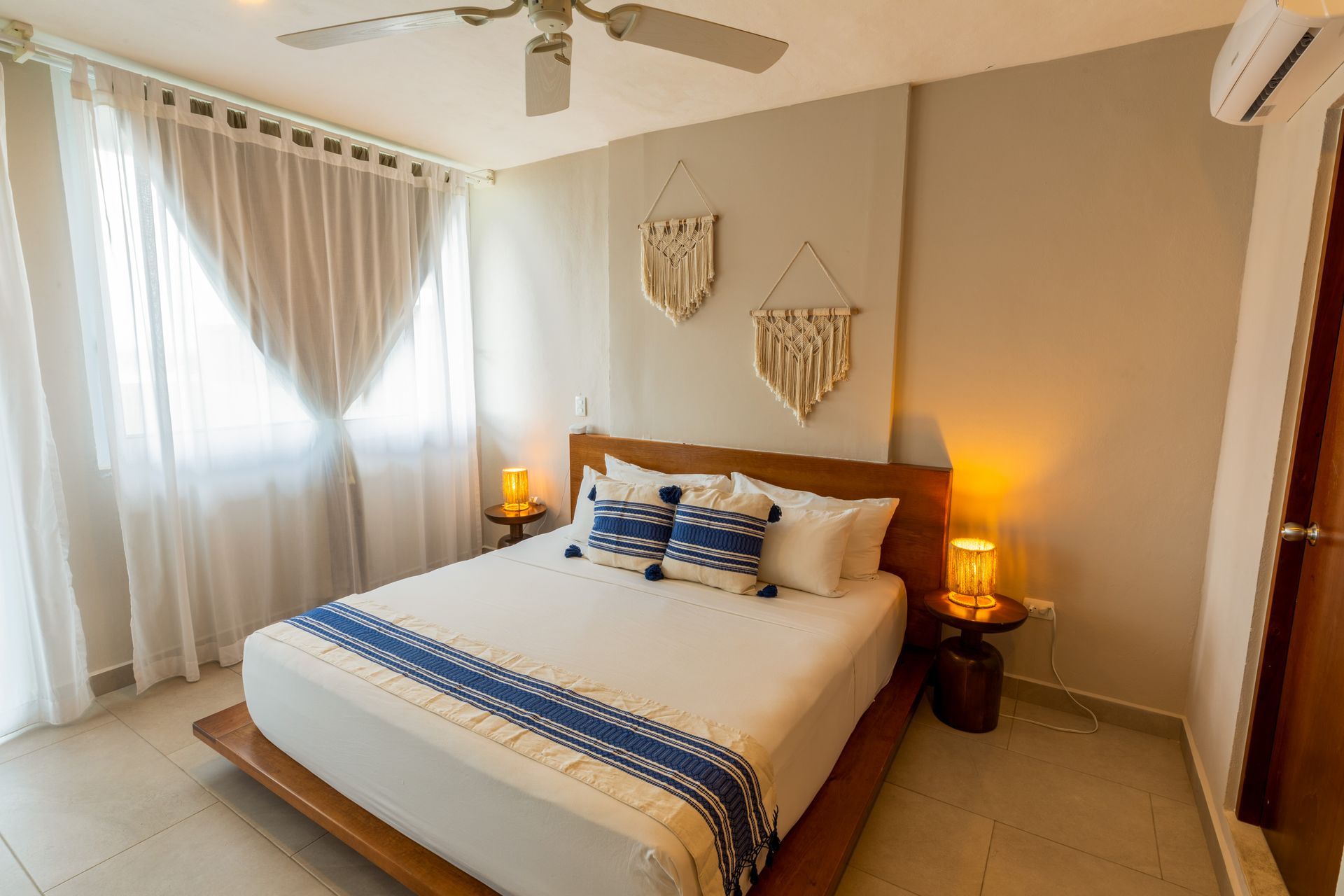 Habitación luminosa con cama king size, detalles en azul, cortinas transparentes y lámparas de noche de luz cálida.