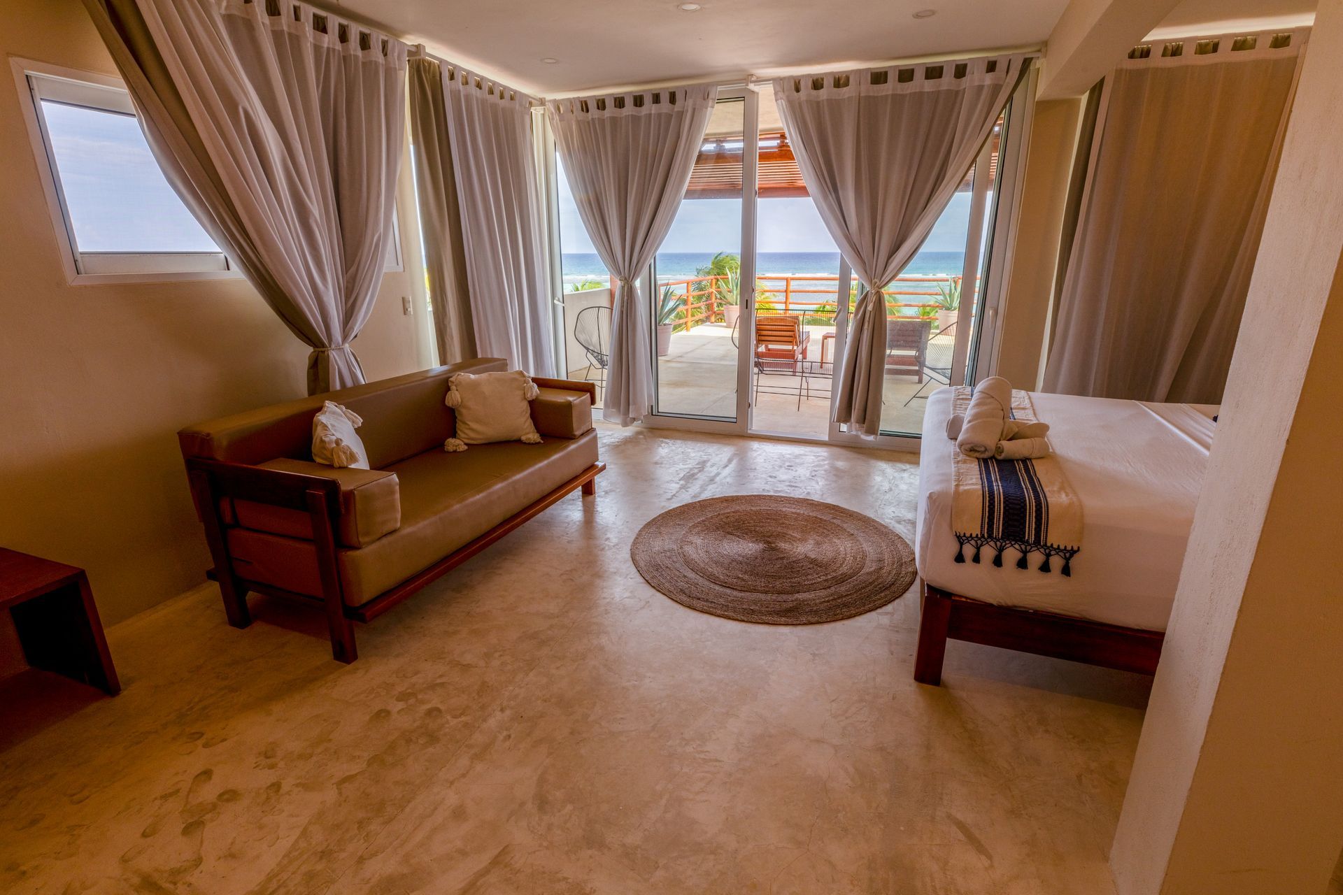 Acogedora sala de estar con sofá, sillón, alfombra y puertas que dan a un balcón con vistas al mar.