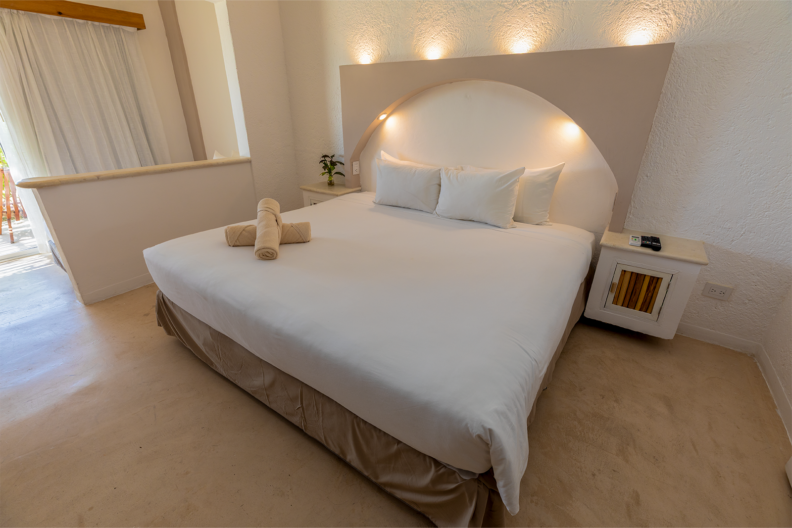 Dormitorio luminoso y minimalista con una cama grande blanca, alfombra beige e iluminación tenue en las paredes.