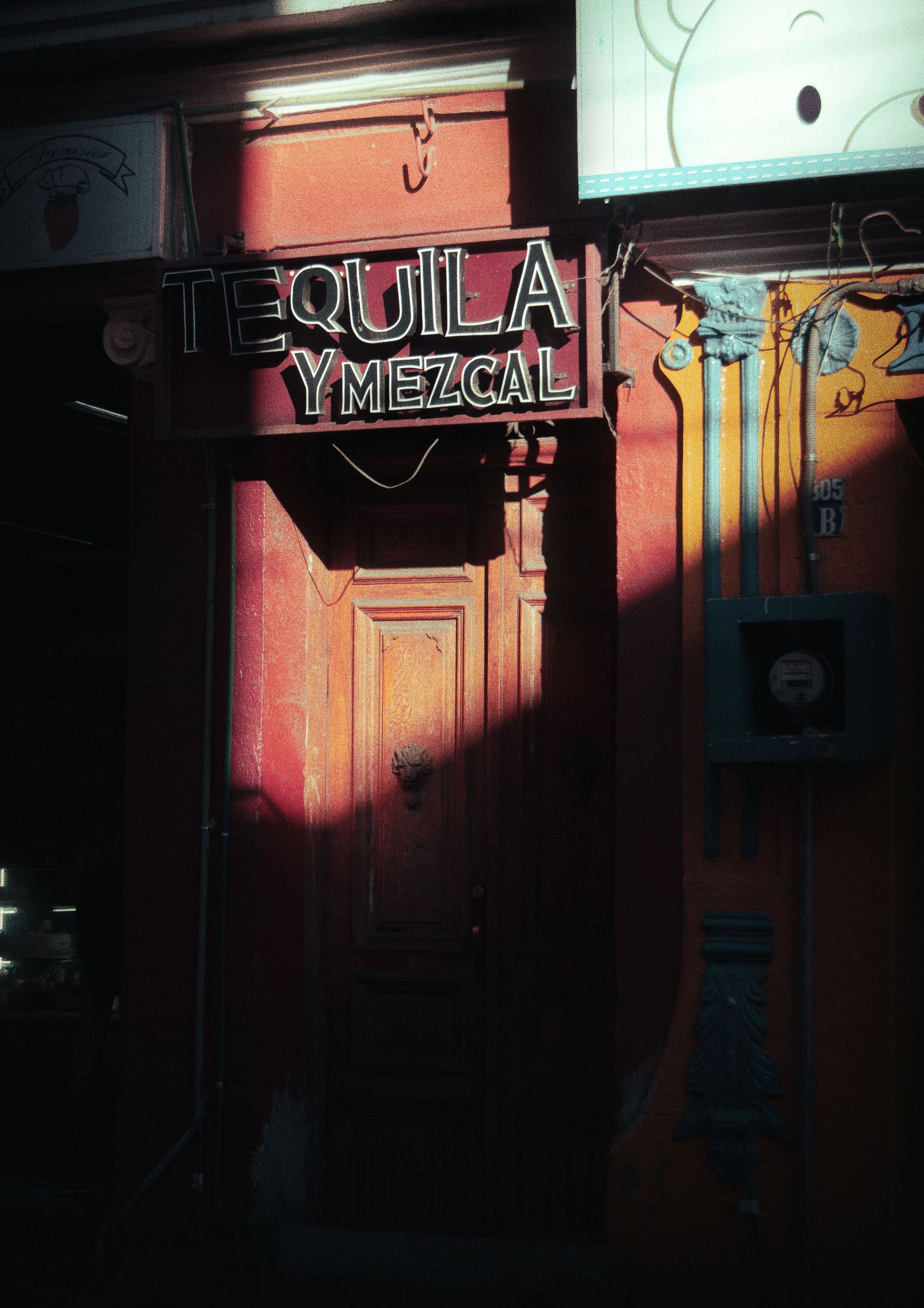 Puerta desgastada con un letrero de “Jalisco Mezcal” bajo la cálida luz del sol y la sombra.