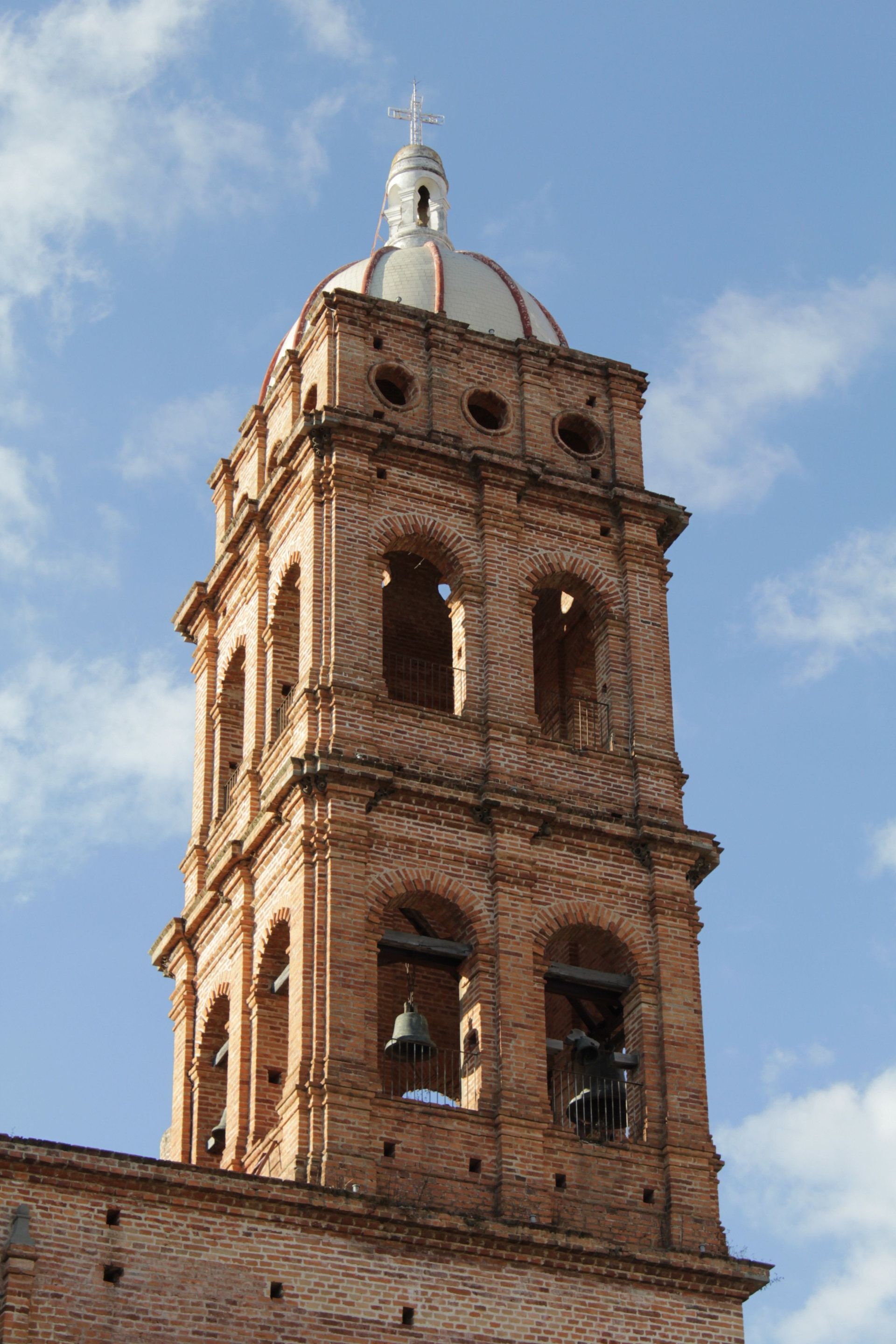 Campanario de iglesia de ladrillo con aberturas arqueadas y una cúpula blanca contra un cielo azul.