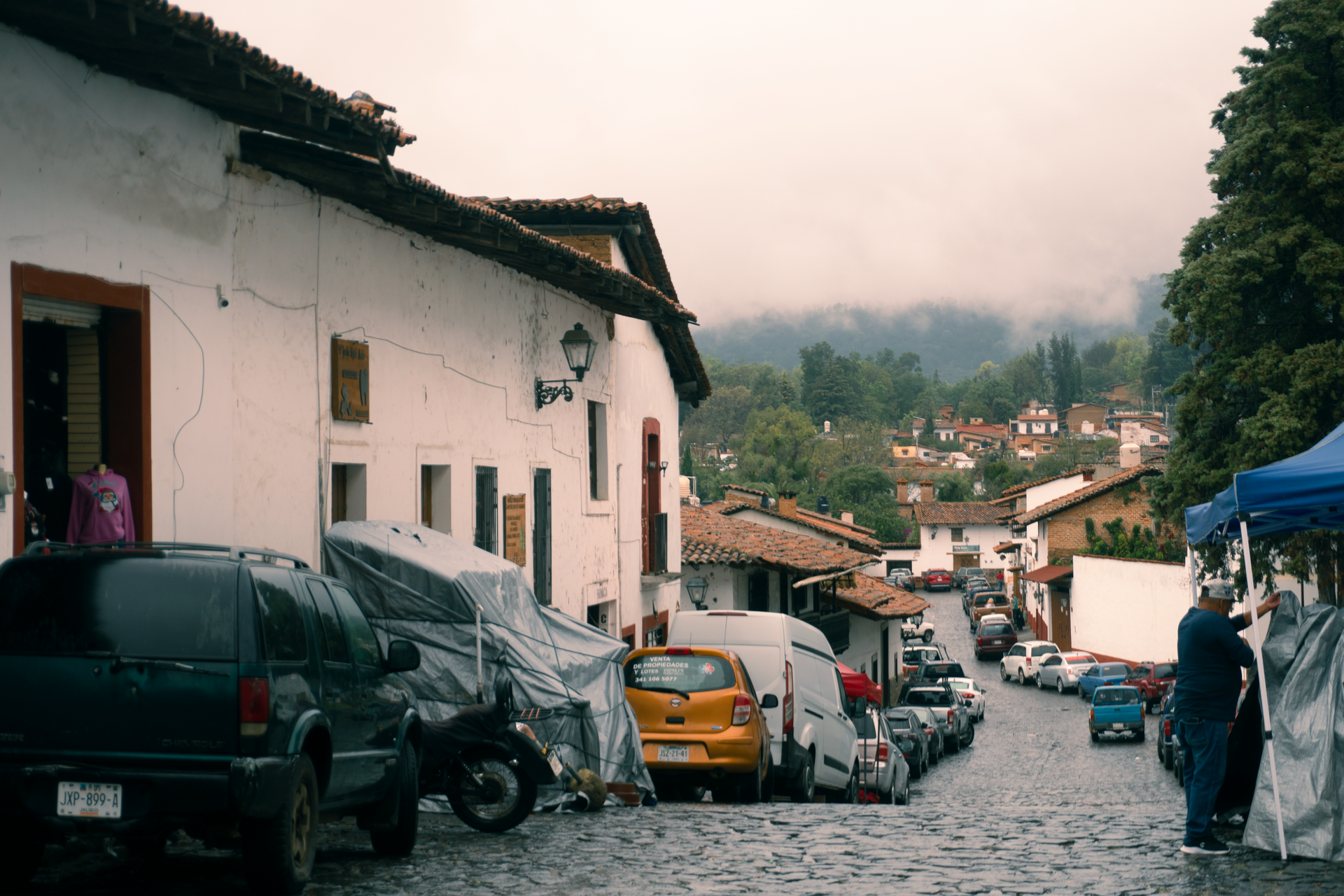 Calle empedrada bordeada de casas blancas y coches aparcados en un pueblo de ladera.