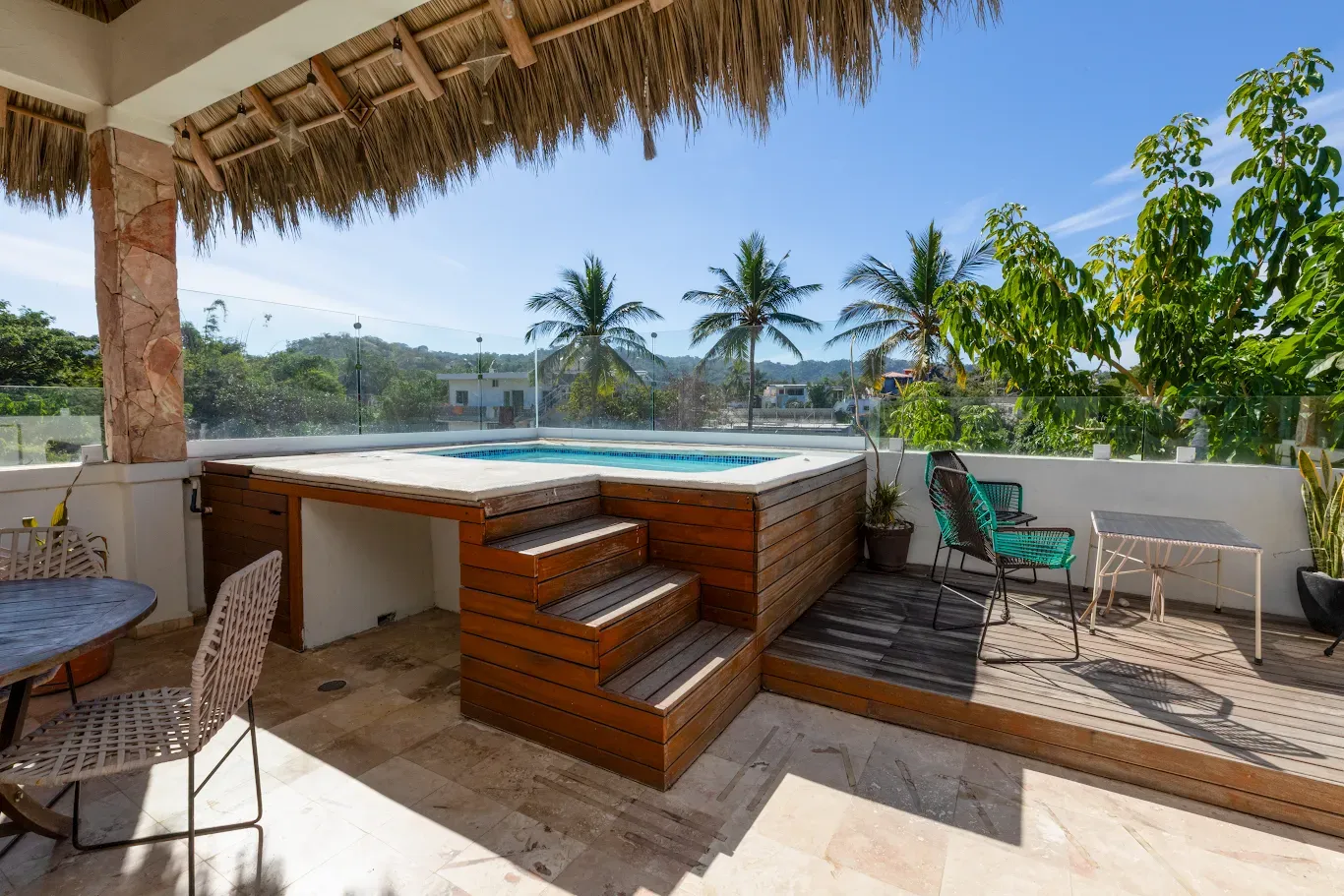 Patio tropical junto a la piscina con taburetes de bar, techo de paja y palmeras con vistas al agua.
