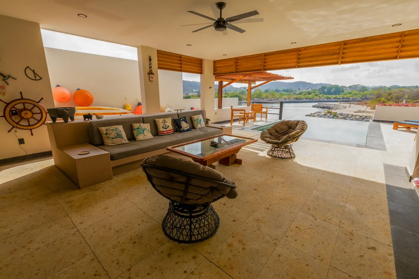 Salón de patio cubierto con sillas de mimbre, sofá y vista al desierto más allá del lado abierto.