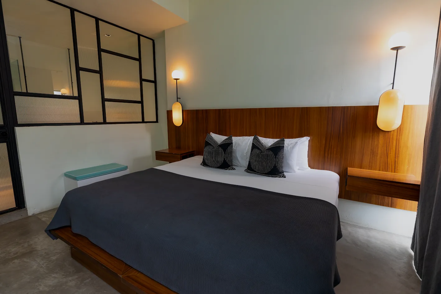 Habitación de hotel moderna con cama king size, ropa de cama gris oscuro, cabecero de madera y lámparas colgantes de luz cálida.