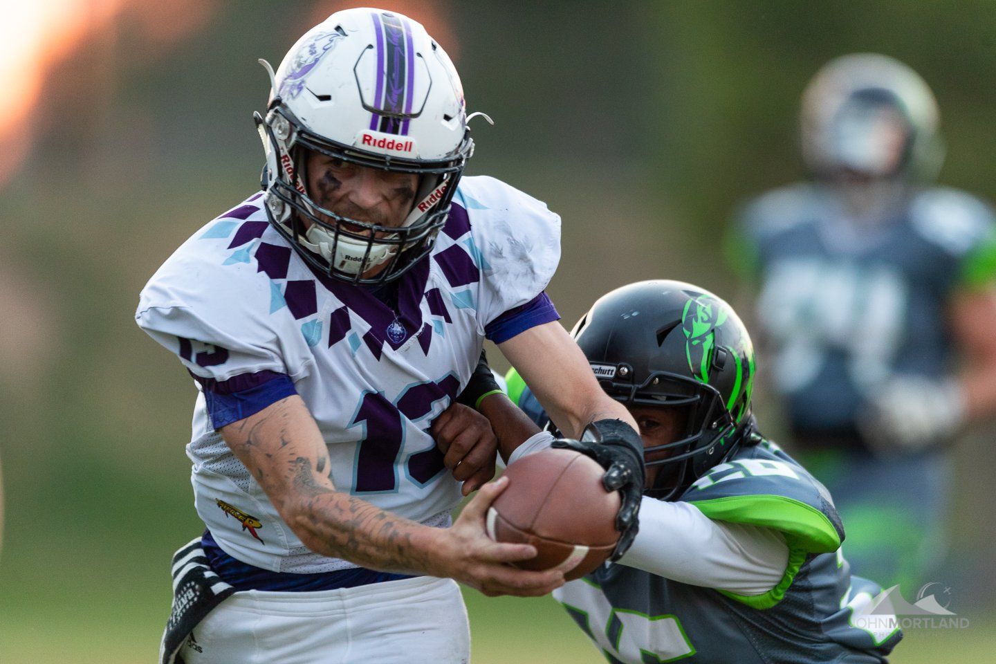 Football player in white and purple uniform tackled by a player in green and gray.