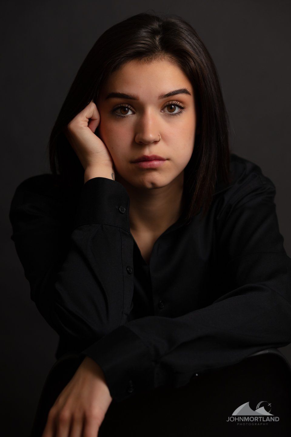 Woman in dark shirt, resting head on hand, looking at the camera.