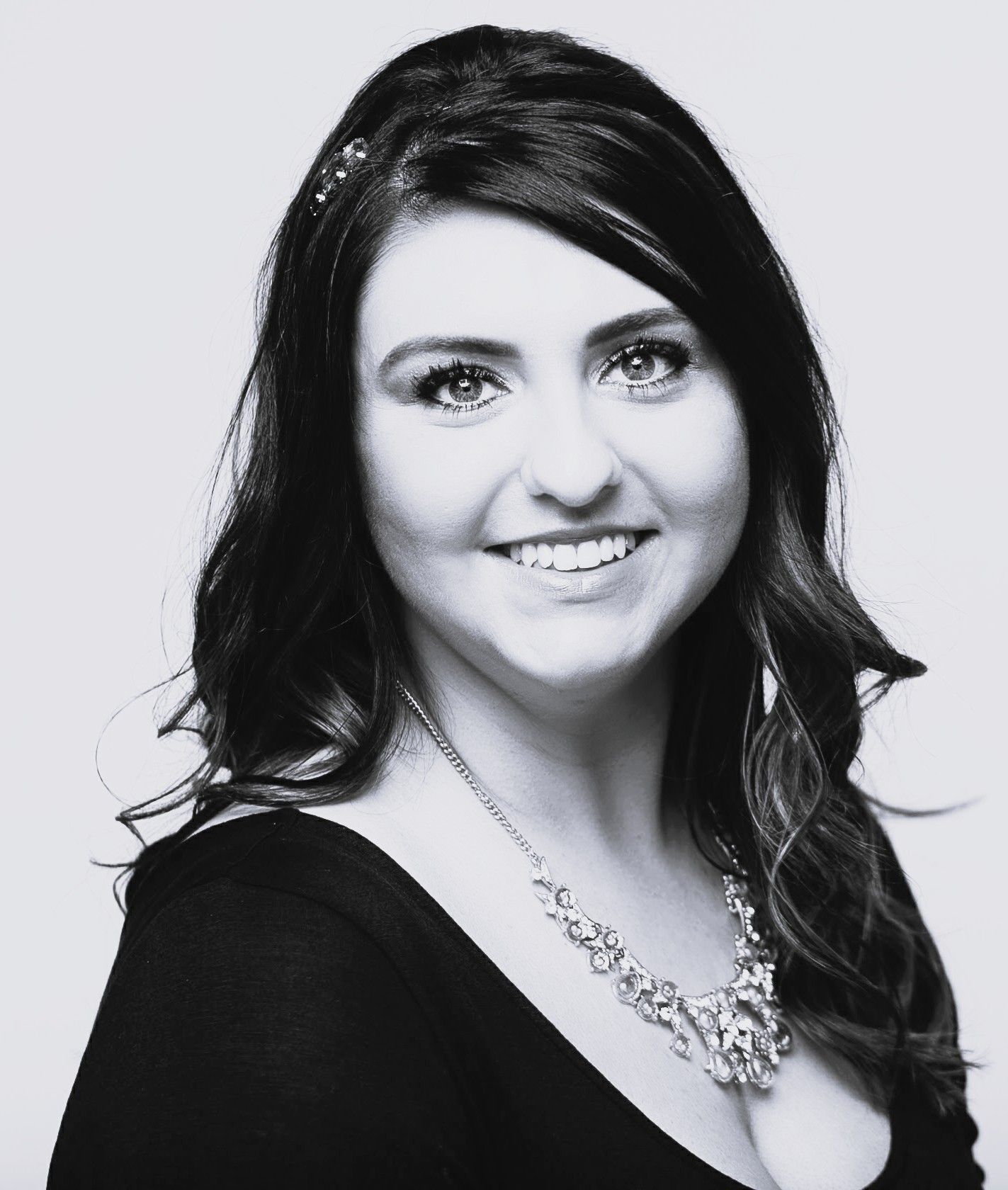 Woman with dark hair smiles, wearing a black top and ornate necklace.