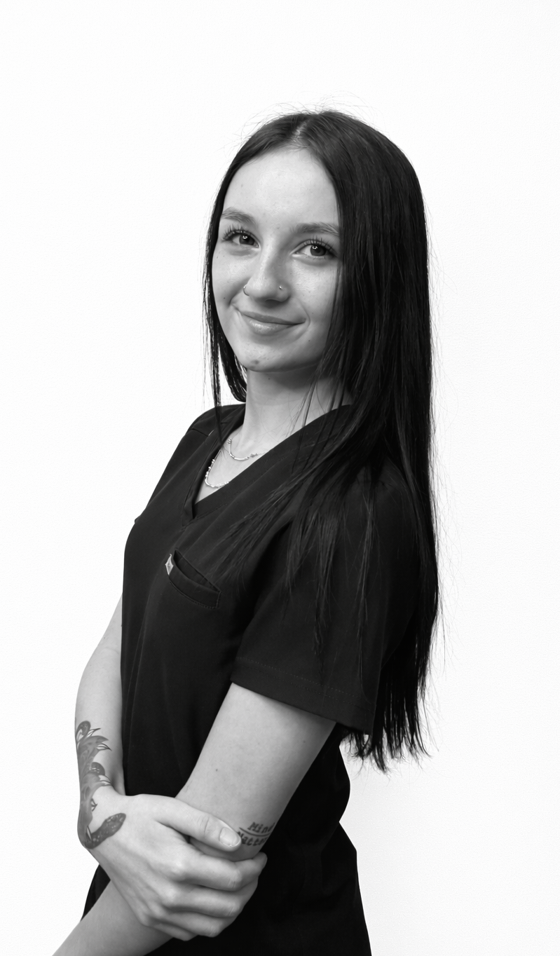 Woman with long dark hair, nose ring, and cross earring, smiling, in front of a white wall.
