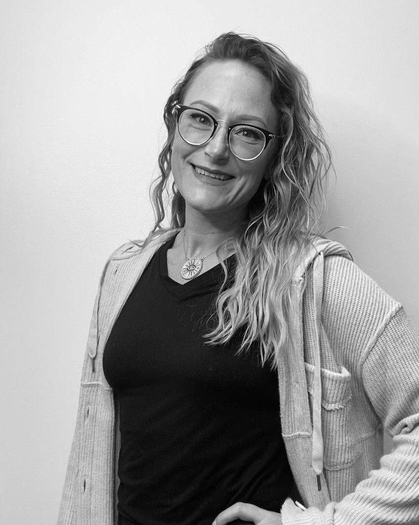 Woman with curly hair and glasses smiles, wearing a black shirt and light-colored cardigan.