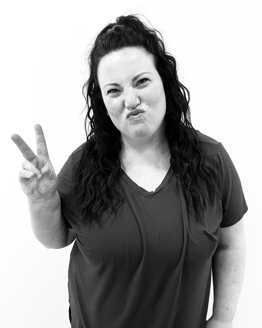 Woman in dark top makes a silly face, holding up two fingers in a peace sign.