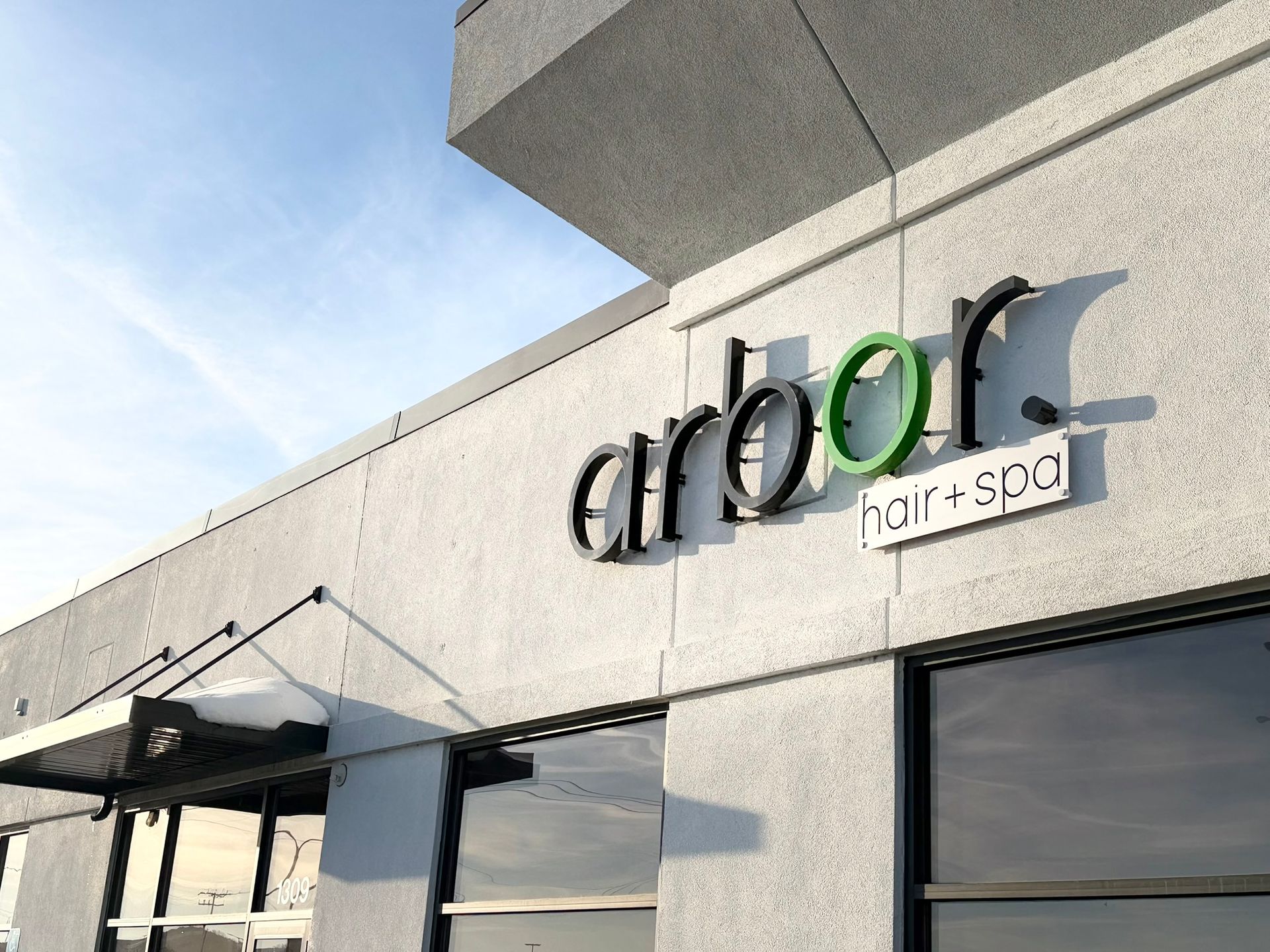 Arbor Hair + Spa storefront sign in black, green, and white on a gray building.