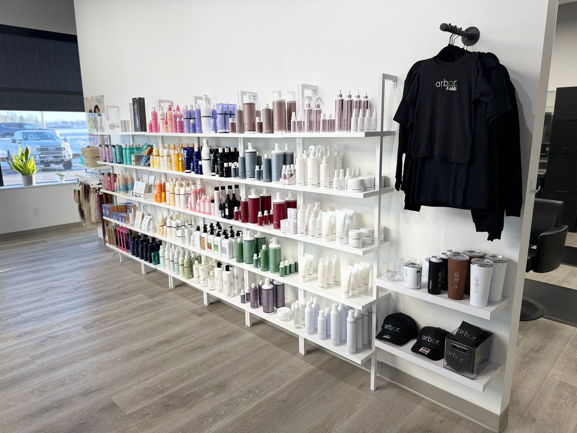 White shelves displaying hair products in a salon. A black shirt hangs beside the shelves.