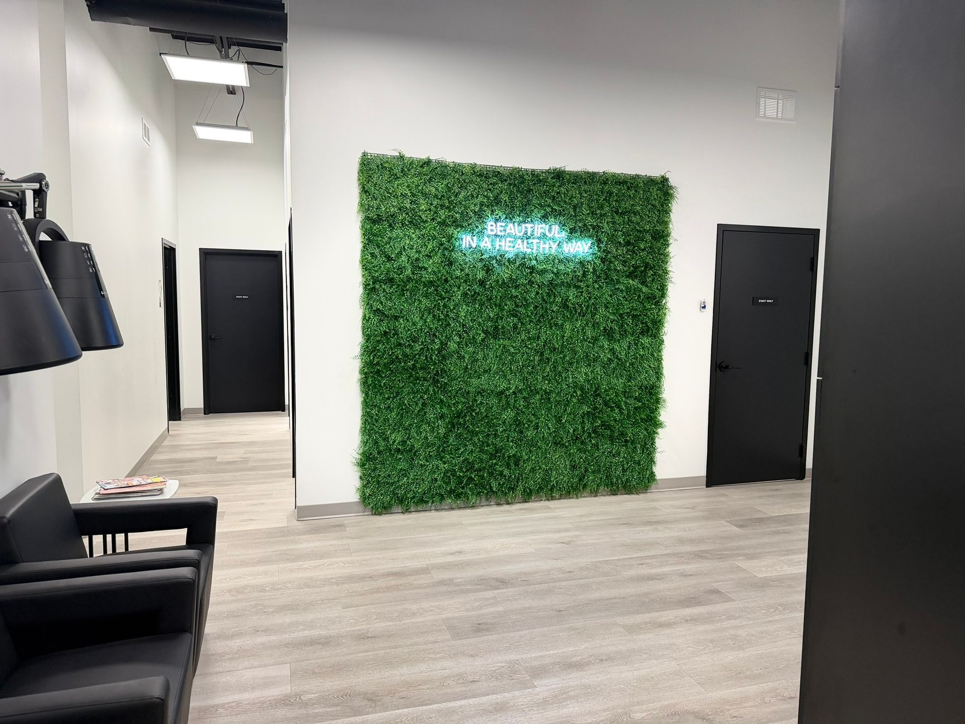 Interior waiting area with green wall, neon sign, black doors, and black chairs.
