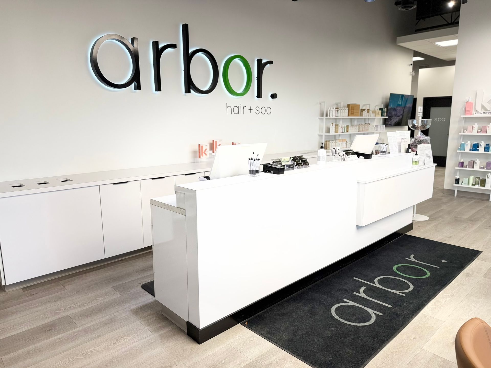 Arbor hair spa reception area: white counter, sign, products, and mat on wooden floor.