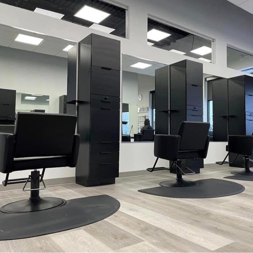 Hair salon interior with black styling chairs, stations, and mirrors. Gray wood-look floors.