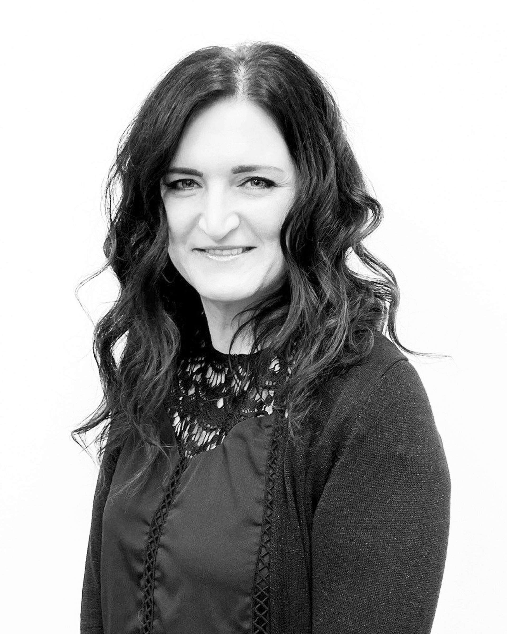 Woman with dark wavy hair smiles, wearing a black top and cardigan.
