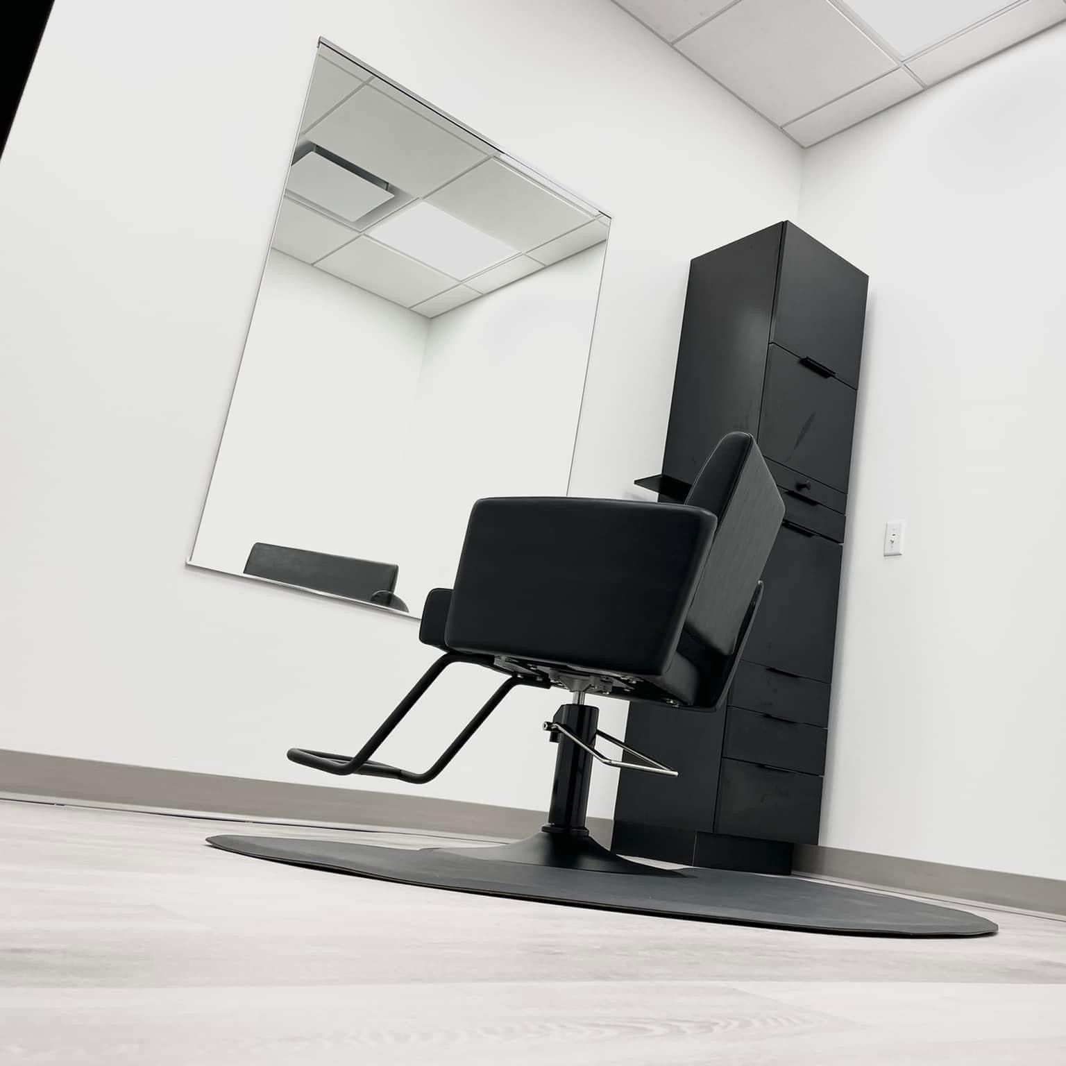 Hair salon station with black chair, mirror, and cabinet against a white wall.