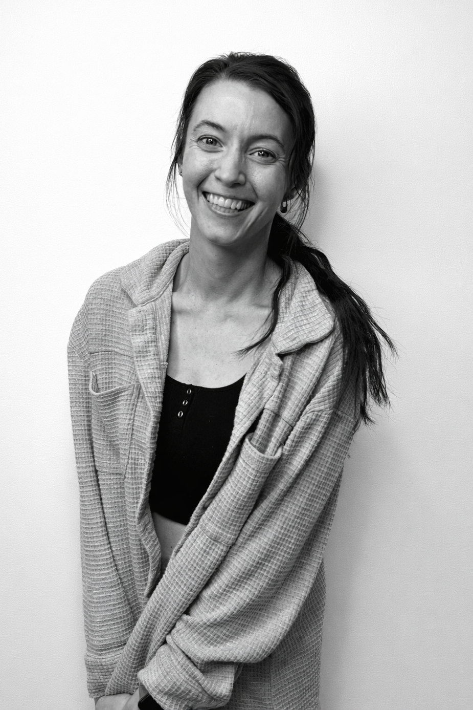 Woman in a black tank top with a logo smiles, wearing striped pants, in front of a white wall.