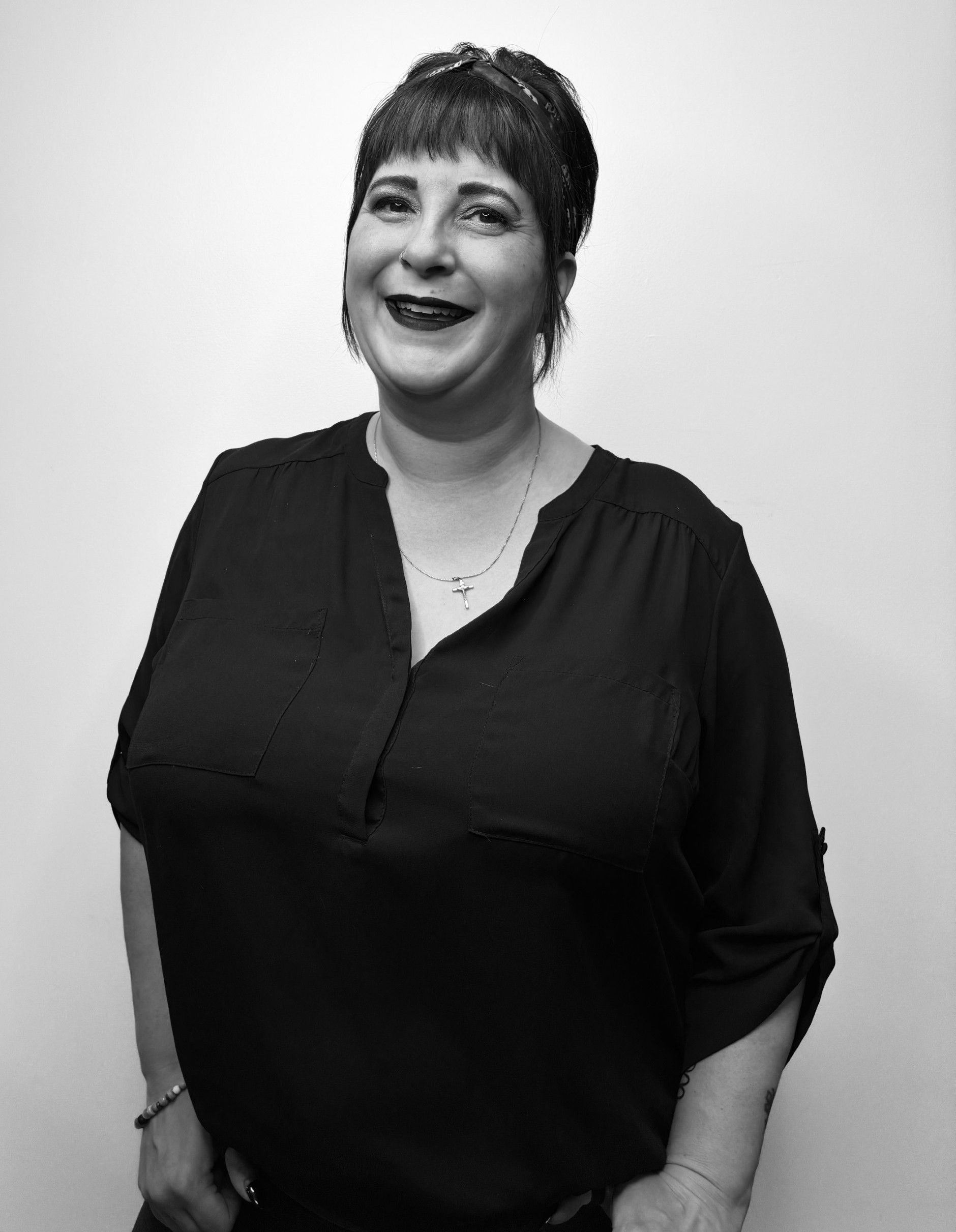 Woman in a dark blazer smiles, holding the lapel. Gray hair, indoor setting.