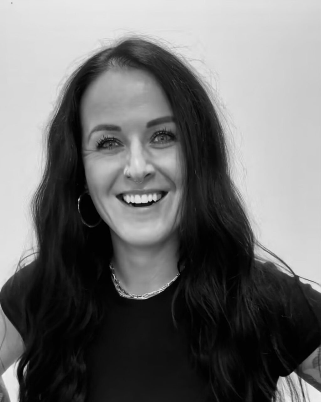 Woman with dark wavy hair smiling, wearing a black shirt and silver necklace.