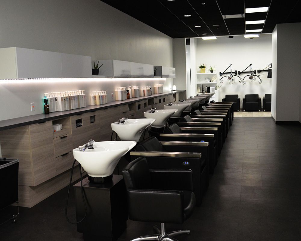 Hair salon interior with several wash stations and chairs. Light walls, dark floor, and black ceiling.