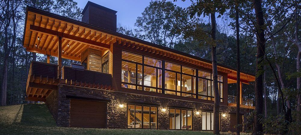 A large house with a lot of windows is surrounded by trees at night.
