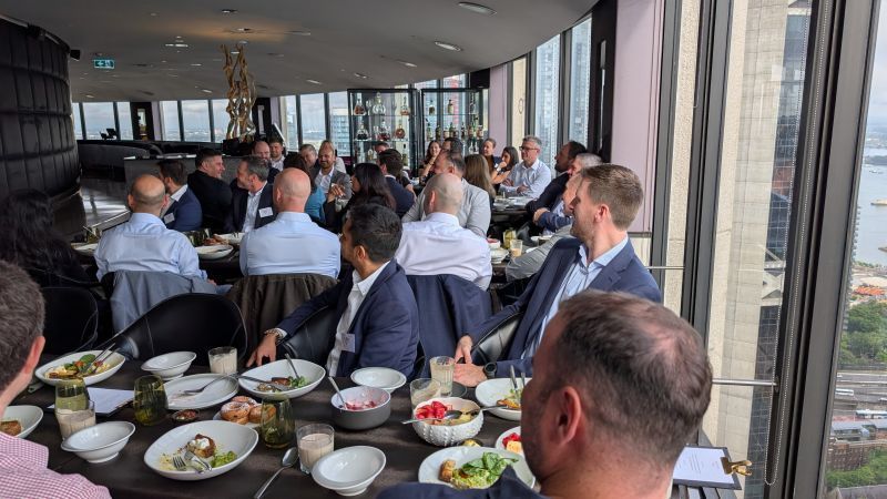 A group of people dining at tables in a high-rise restaurant with floor-to-ceiling windows overlooking a city.