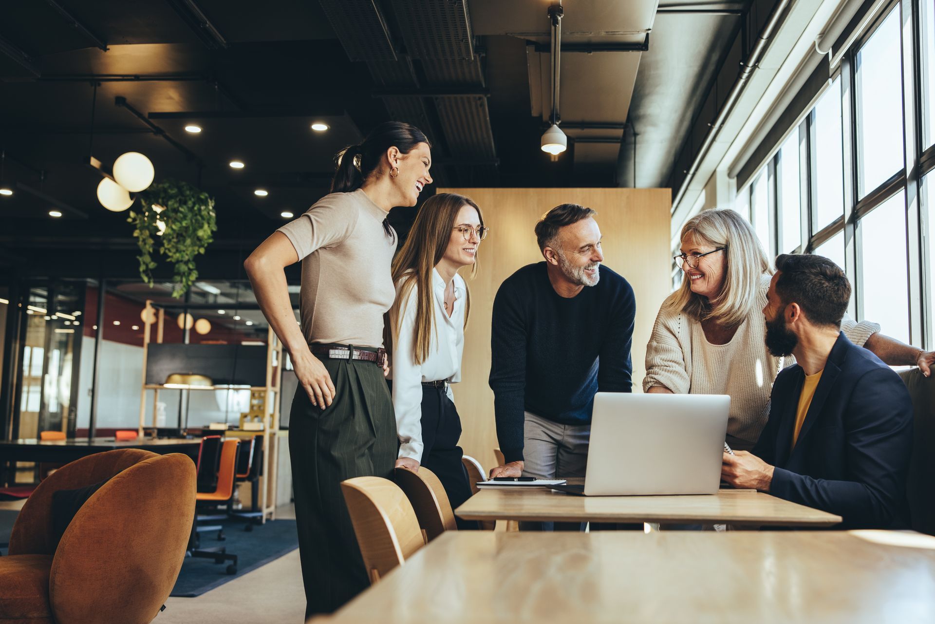 Group of people collaborating around a laptop in a modern office space, smiling.