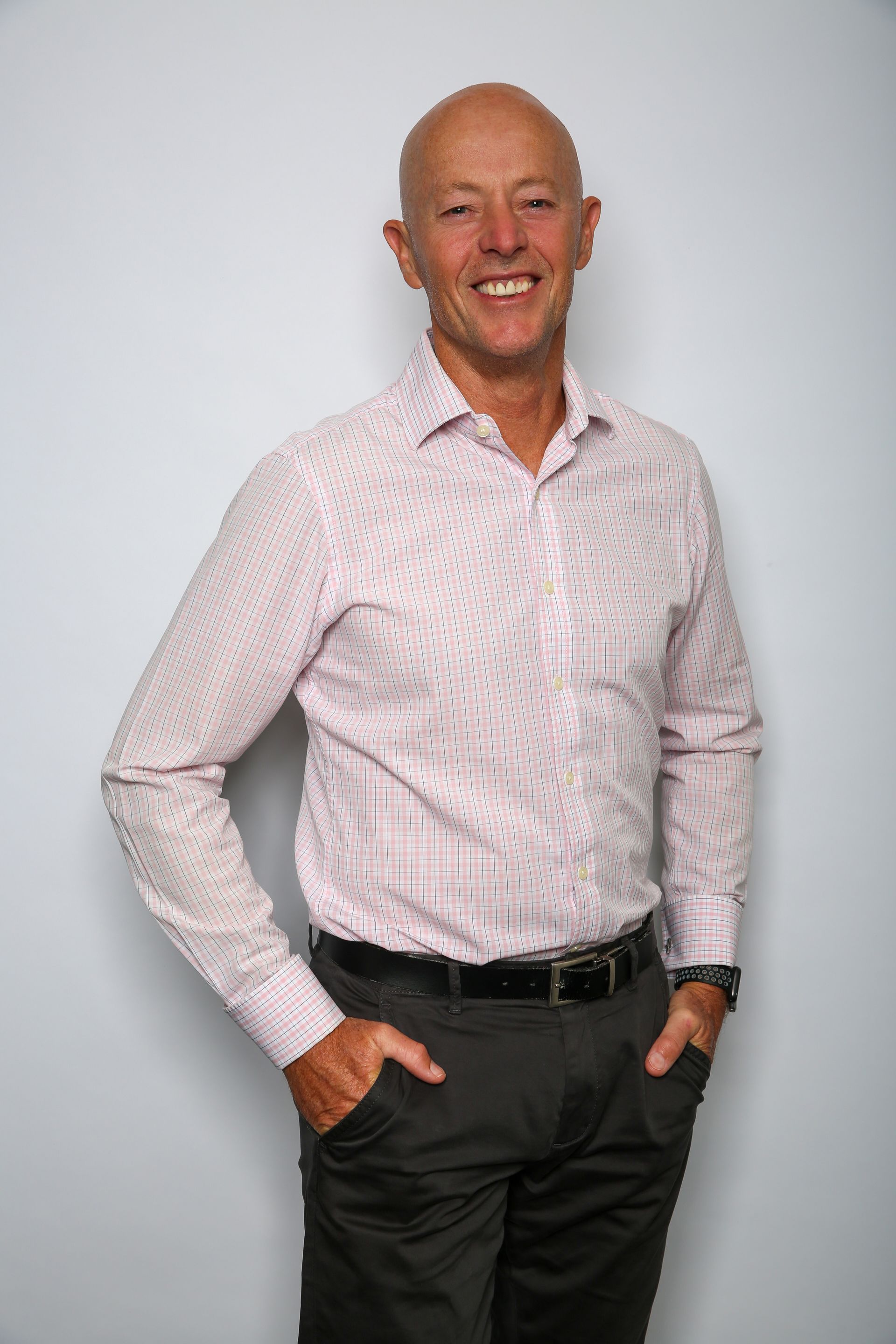 A smiling person wearing a patterned button-down shirt and dark pants, standing with hands in their pockets.