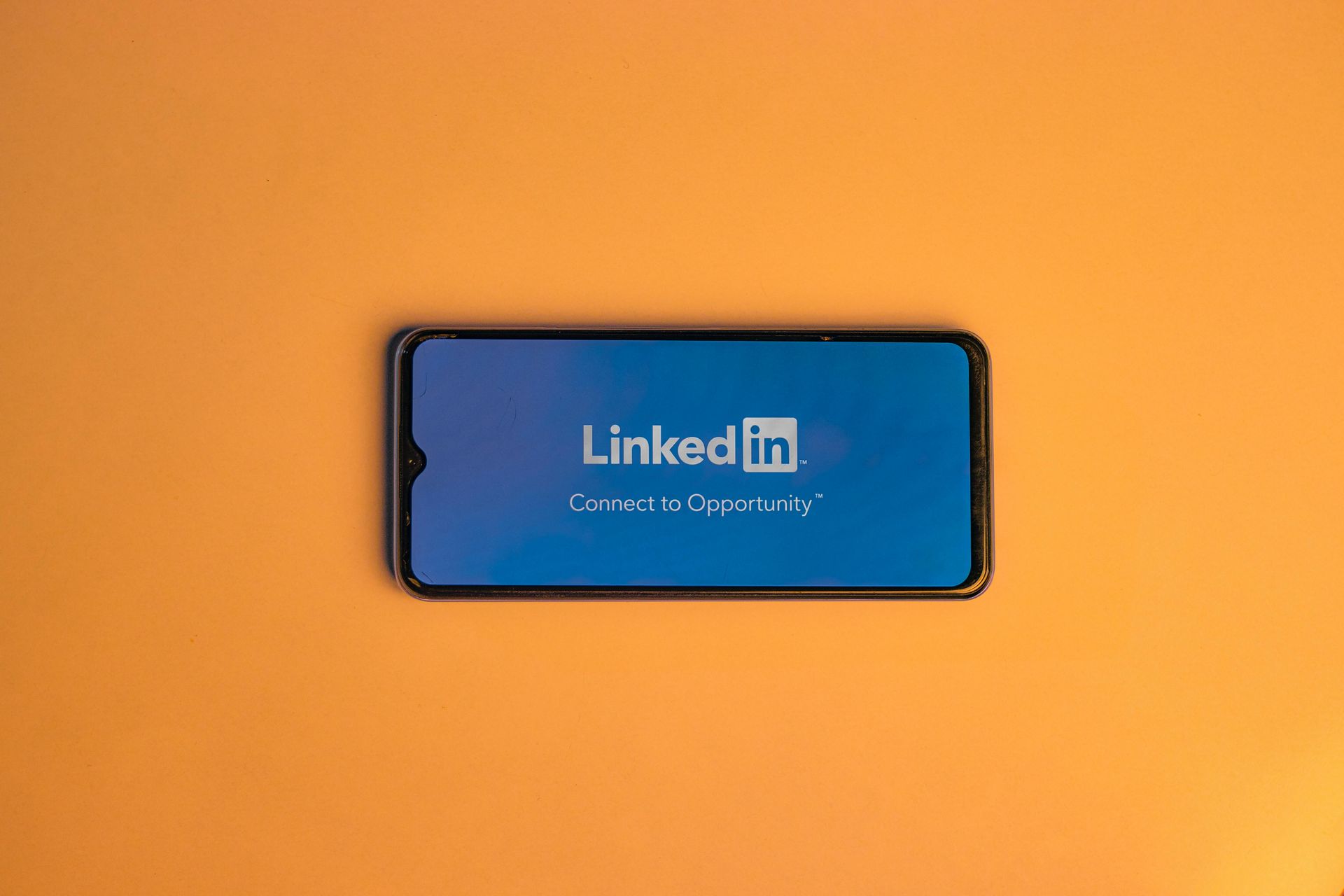Smartphone displaying the LinkedIn logo on a blue screen, set against an orange background.