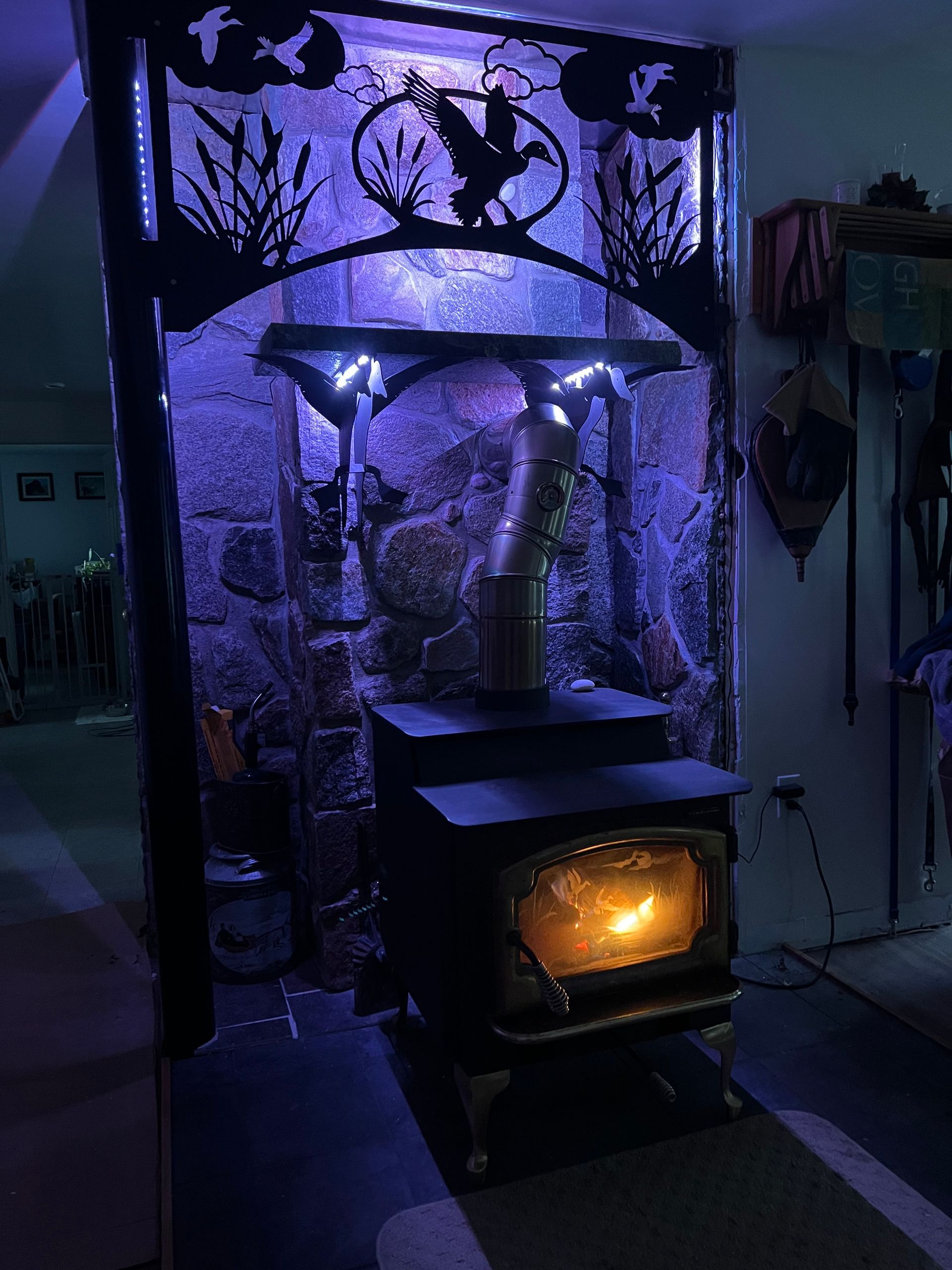 A wood-burning stove glows with fire inside a stone hearth, illuminated by purple ambient lighting and wildlife decor.