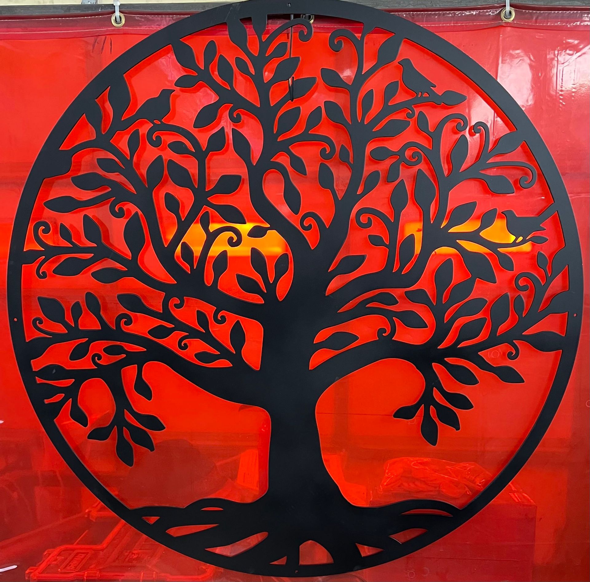 Black metal wall art of a tree of life with birds in its branches, mounted against a vibrant red translucent background.