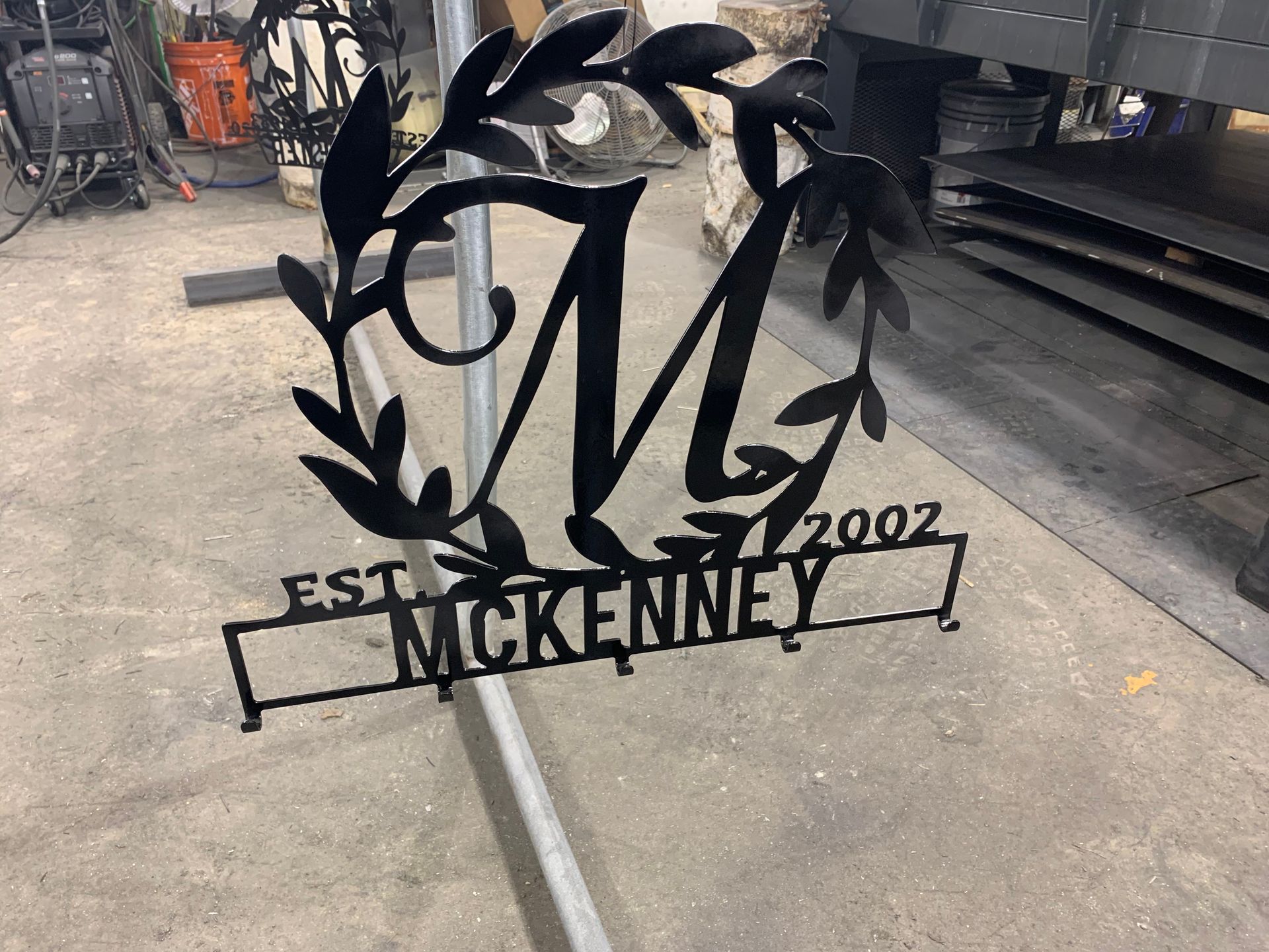 A black metal monogram sign featuring the letter M inside a wreath, labeled