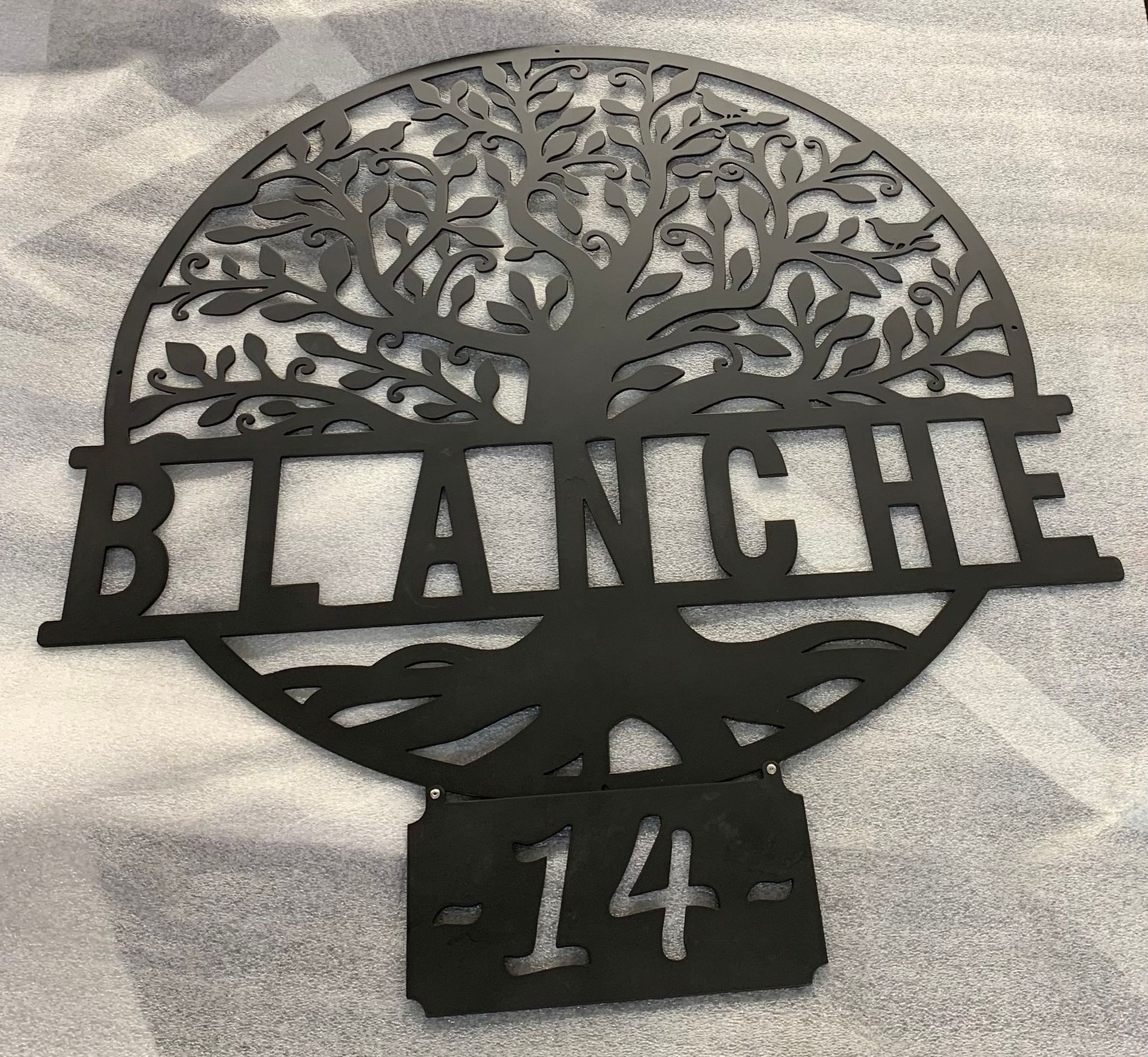A black metal sign featuring a tree silhouette, the name