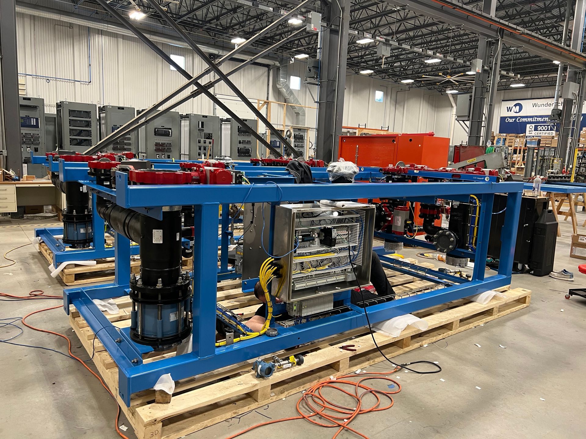 Industrial equipment on a blue metal frame and wooden pallet sits in a large, well-lit manufacturing facility.