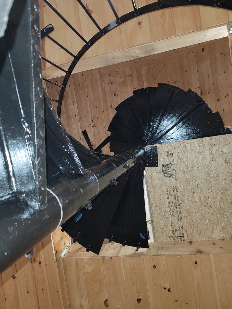 A top-down view of black spiral stairs inside a light wood-paneled stairwell.