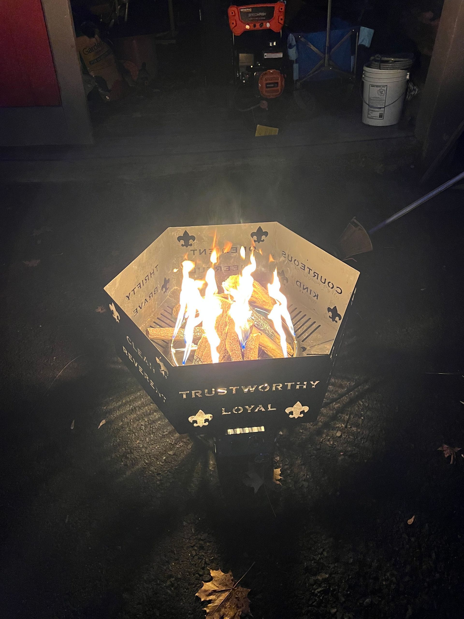 A hexagonal fire pit glowing with flames, decorated with Boy Scout symbols and the words