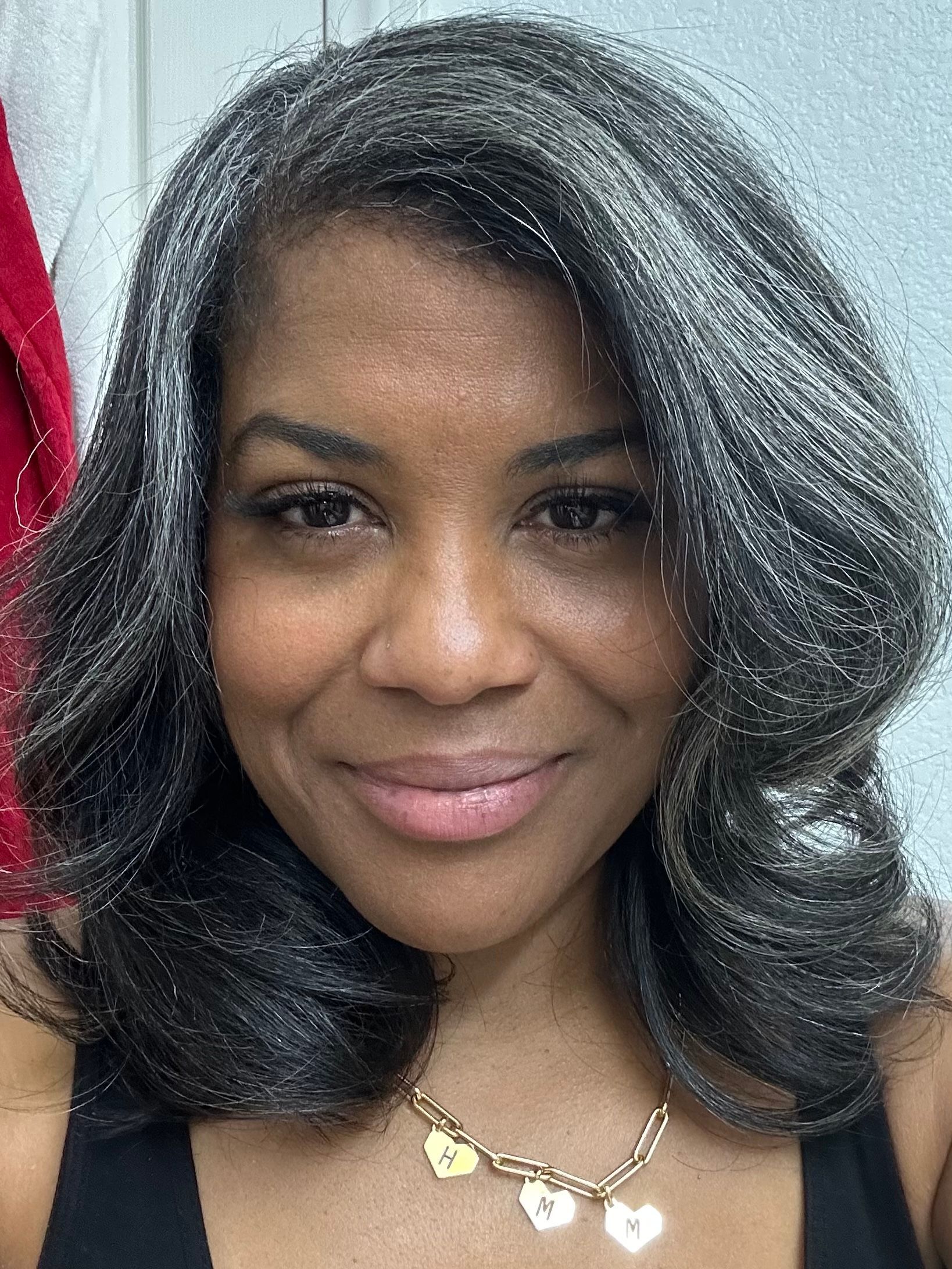 A woman with gray hair is smiling and wearing a necklace.