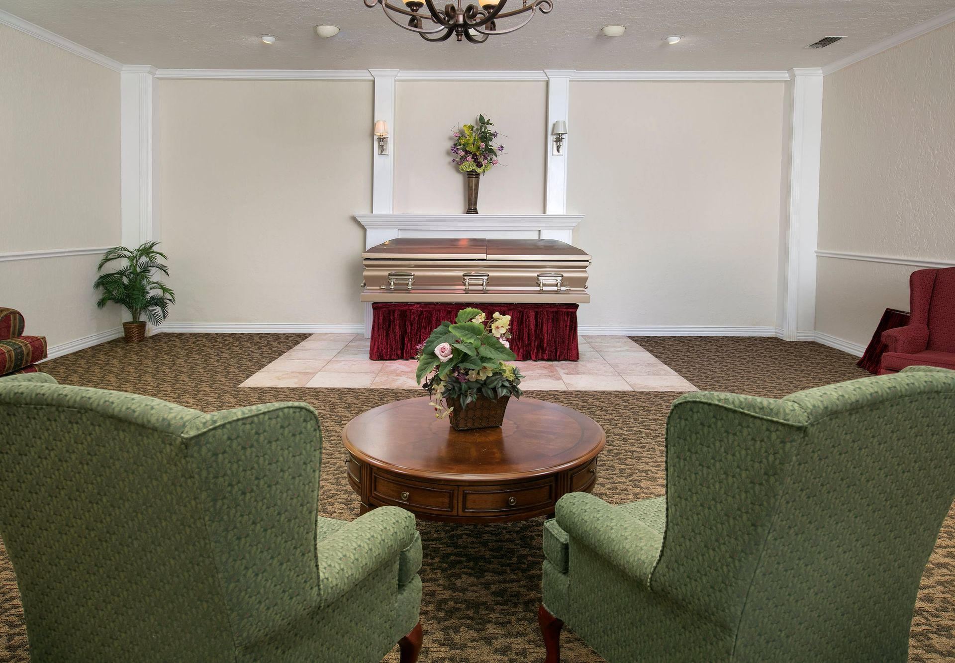 A living room with green chairs and a coffin in the background