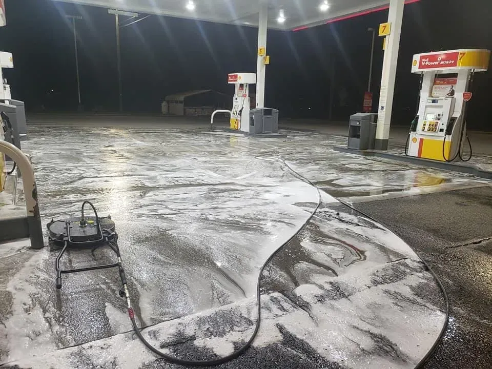 Gas station being cleaned with a pressure washer; concrete covered in soapy foam.