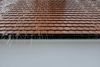 Rain falling off a brown tile roof into a white gutter and wall.