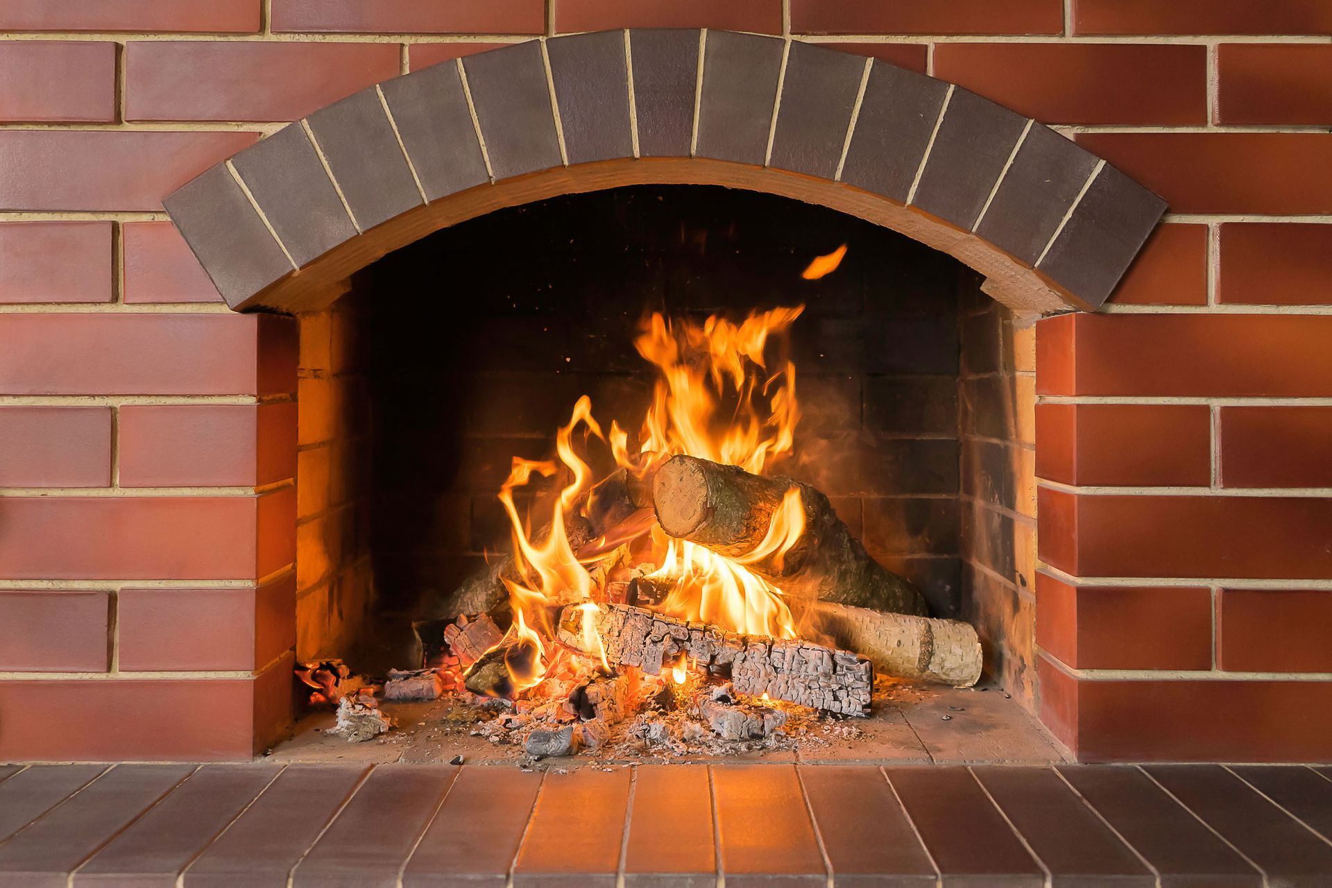Fire burning in a brick fireplace, flames, logs, and embers glowing.