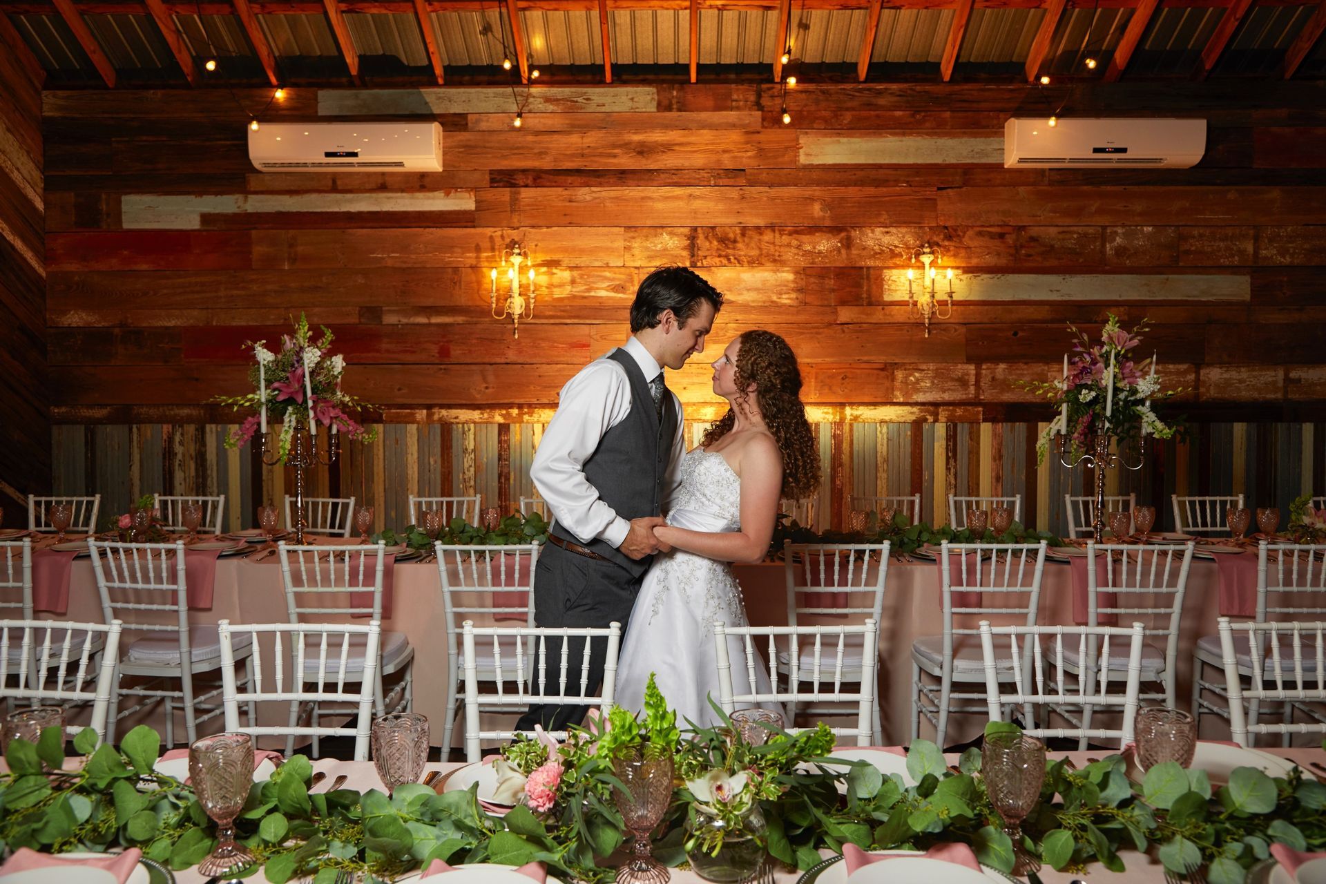A bride and groom are kissing in front of a long table at a wedding reception.