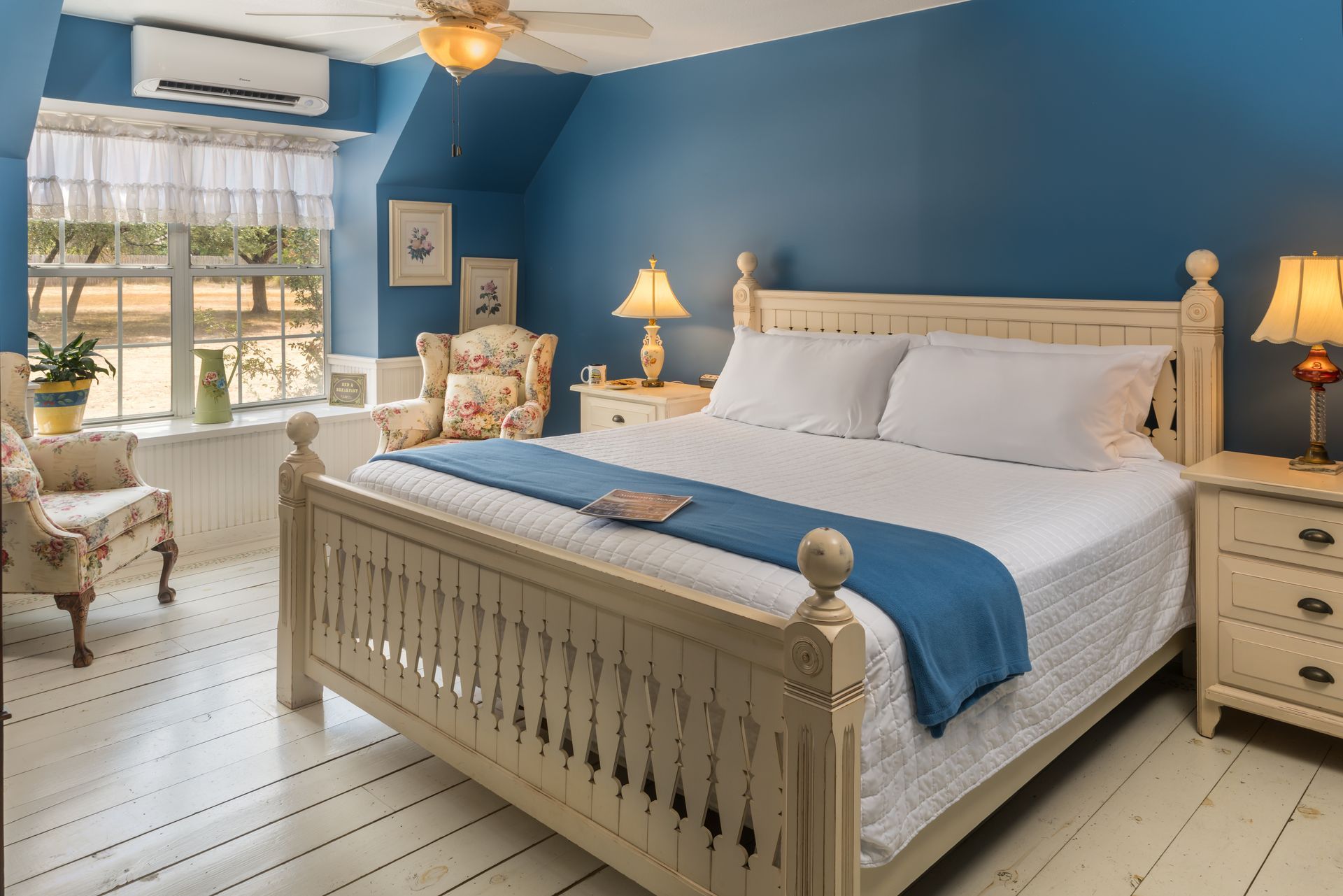 A bedroom with a bed , chair , nightstand , lamps and blue walls.