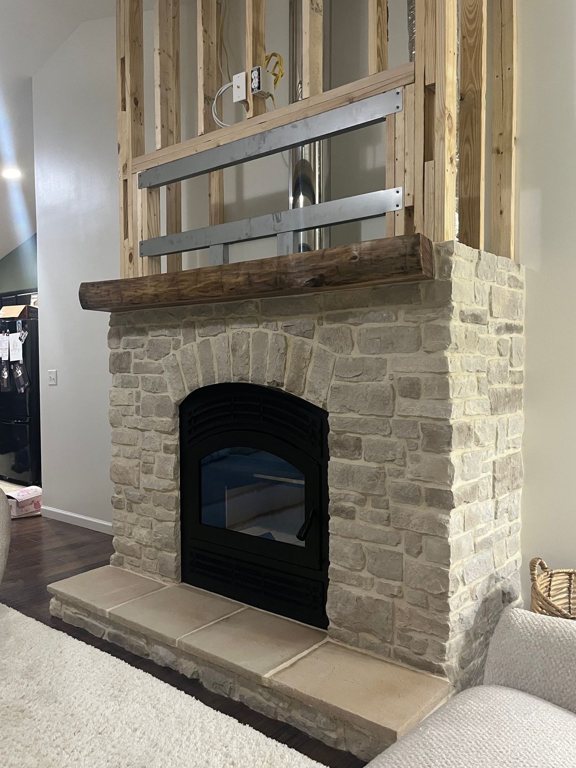 Stone fireplace with black arched insert and wood mantel in a partially renovated room