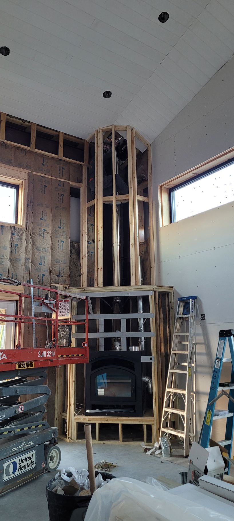 Interior of a room under construction with exposed framing, ladder, scaffolding, and windows