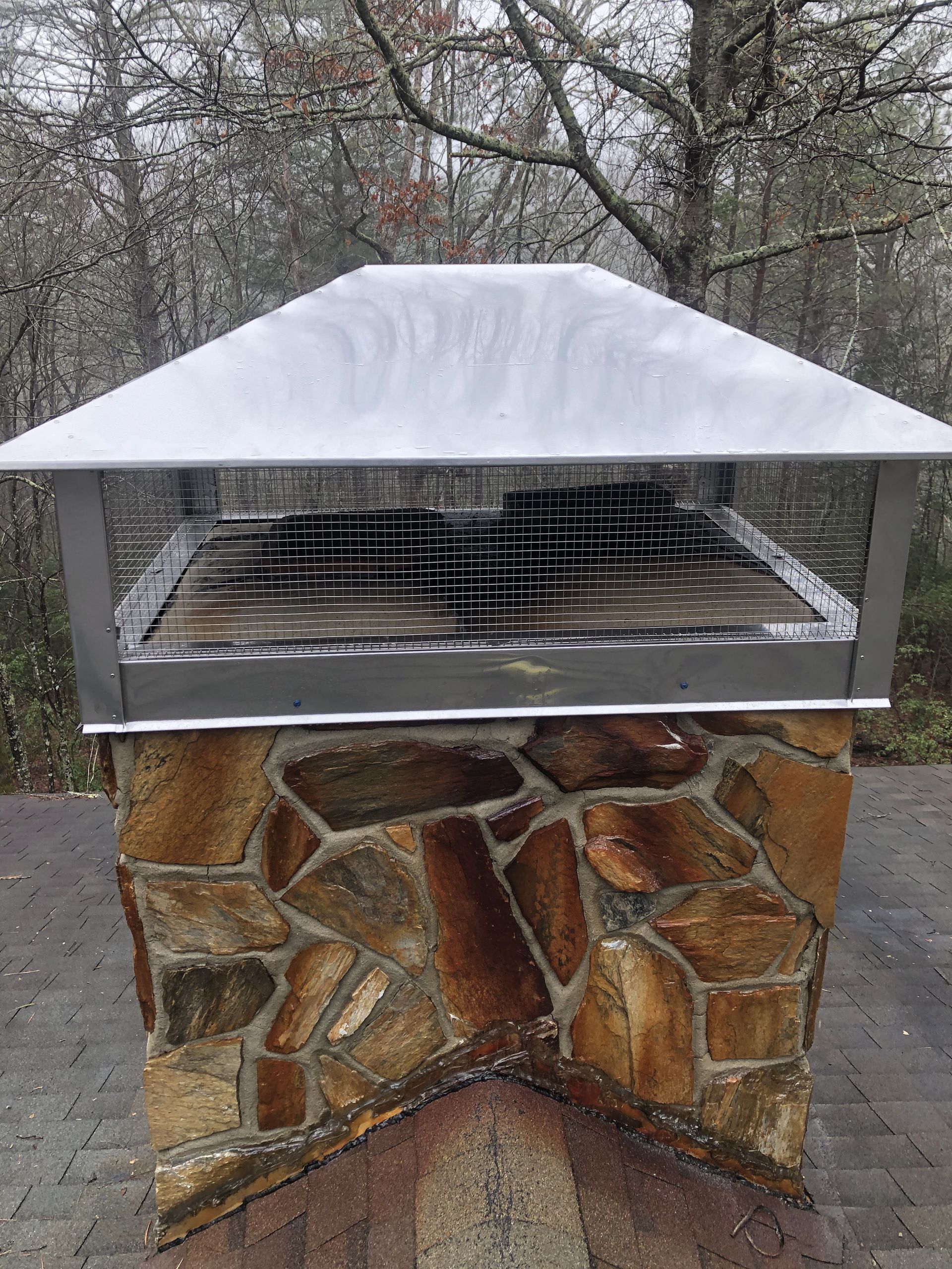 Snow-covered outdoor barbecue grill with stone base and metal top in a yard