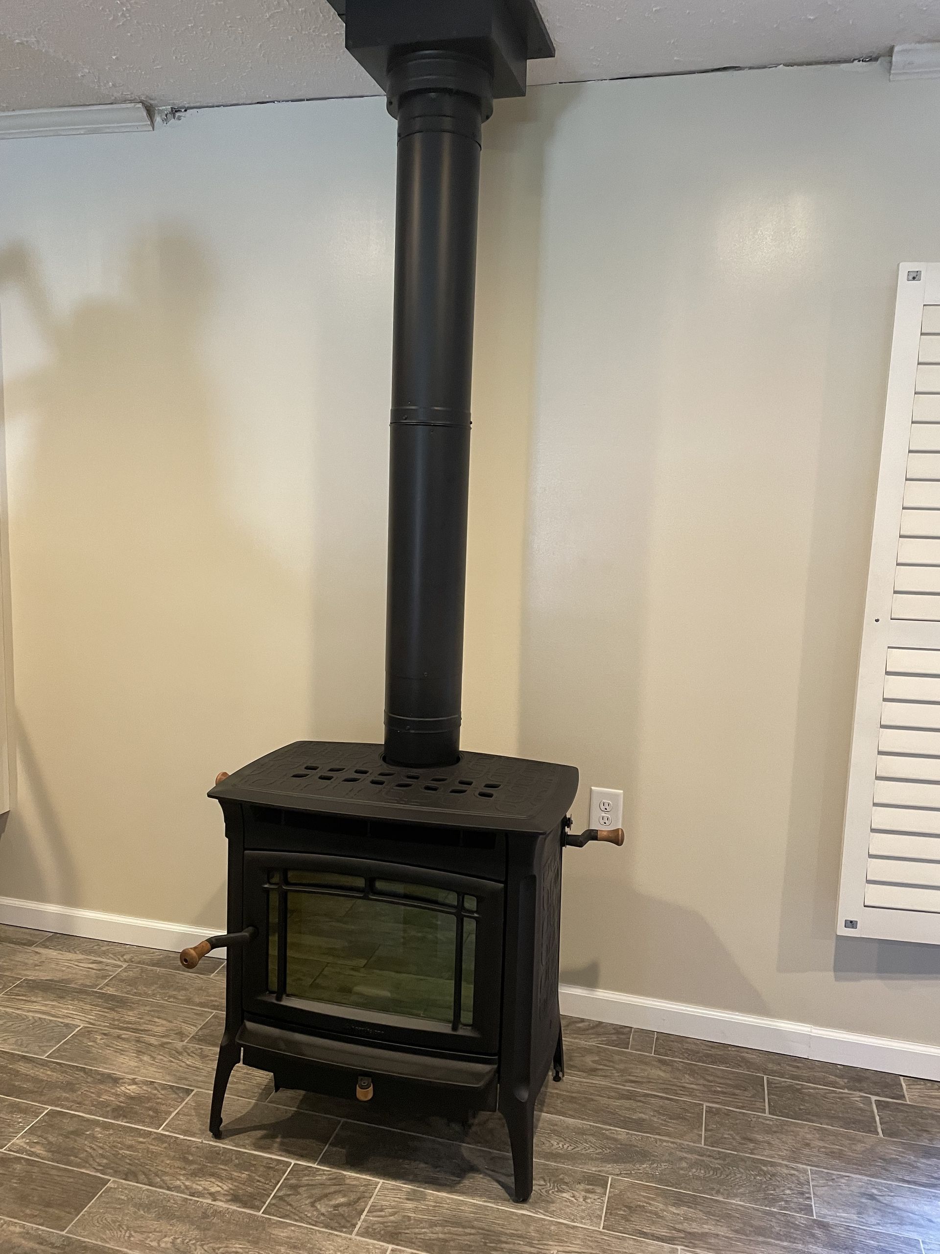 Black wood stove with a tall chimney pipe against a white wall in a small room
